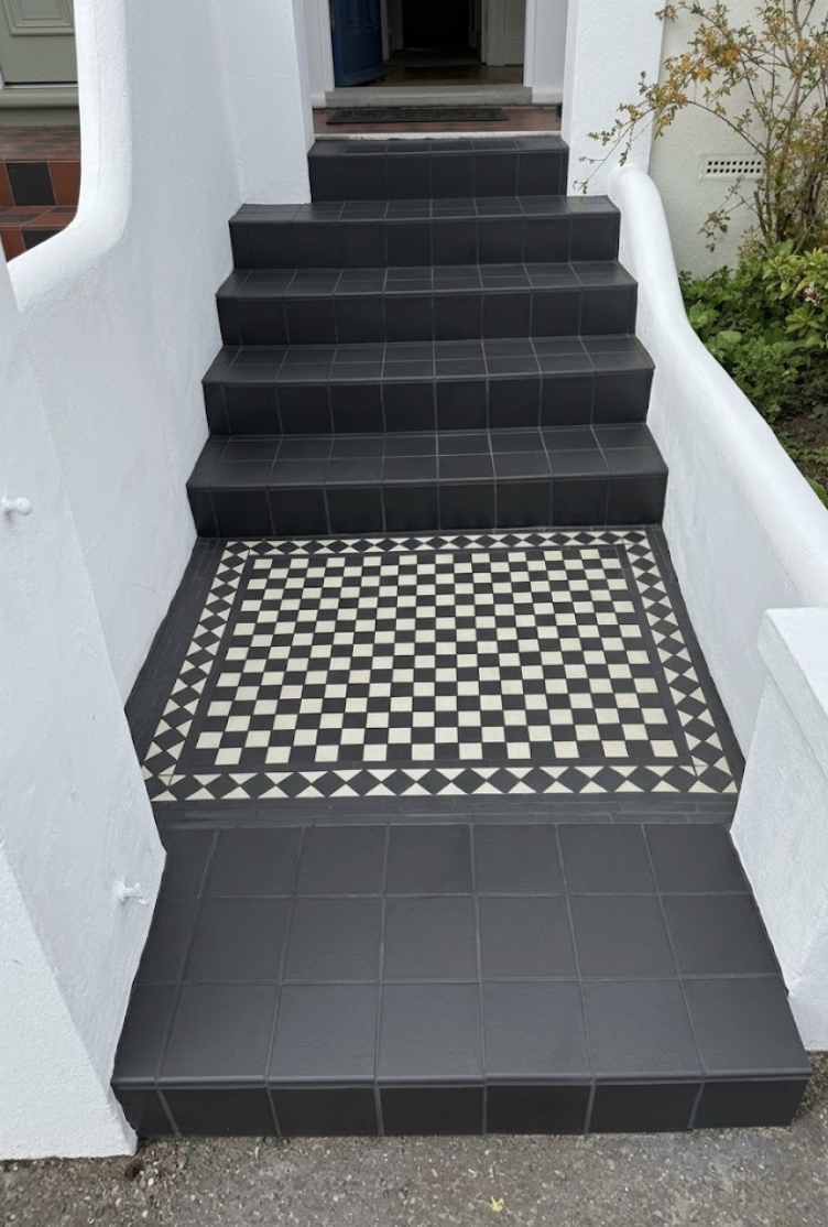 Bright front porch featuring black non-slip steps and a decorative checkerboard mosaic tile landing.