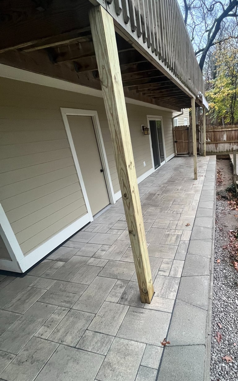 Backyard patio with grey stone pavers installed underneath a raised wooden deck.