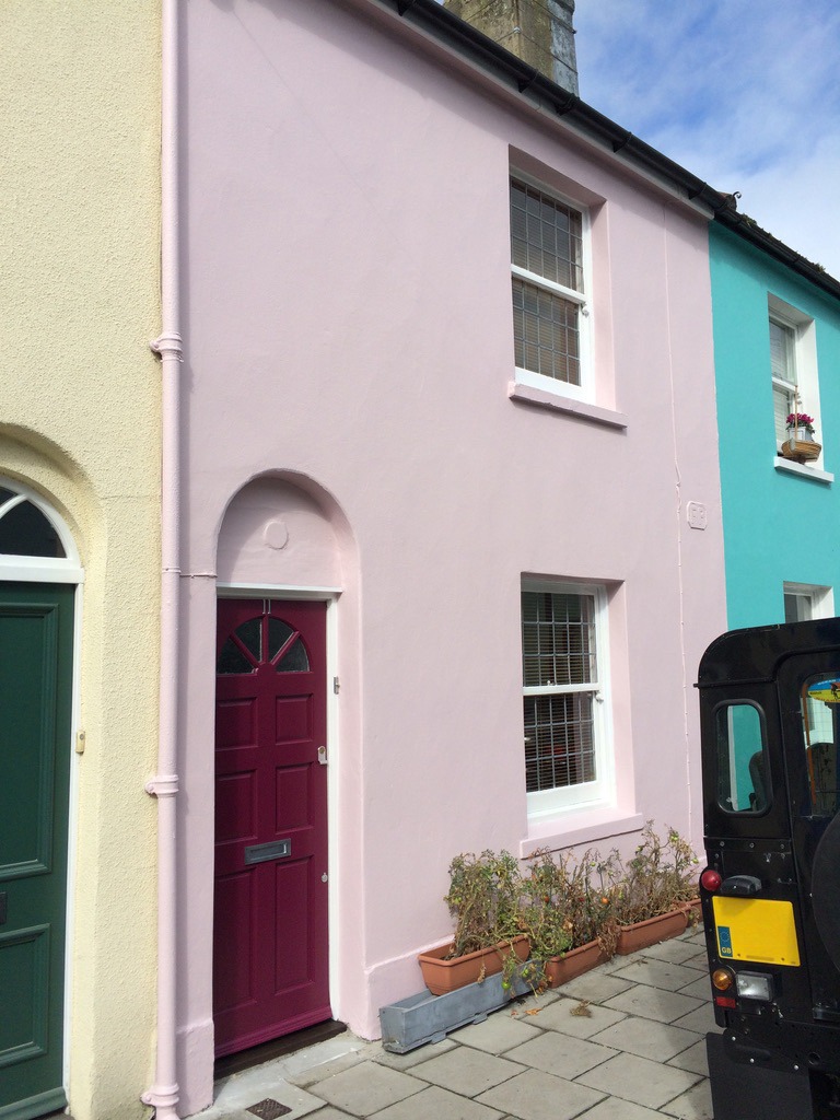 A Brighton pink terraced house with a burgundy door and white sash windows.