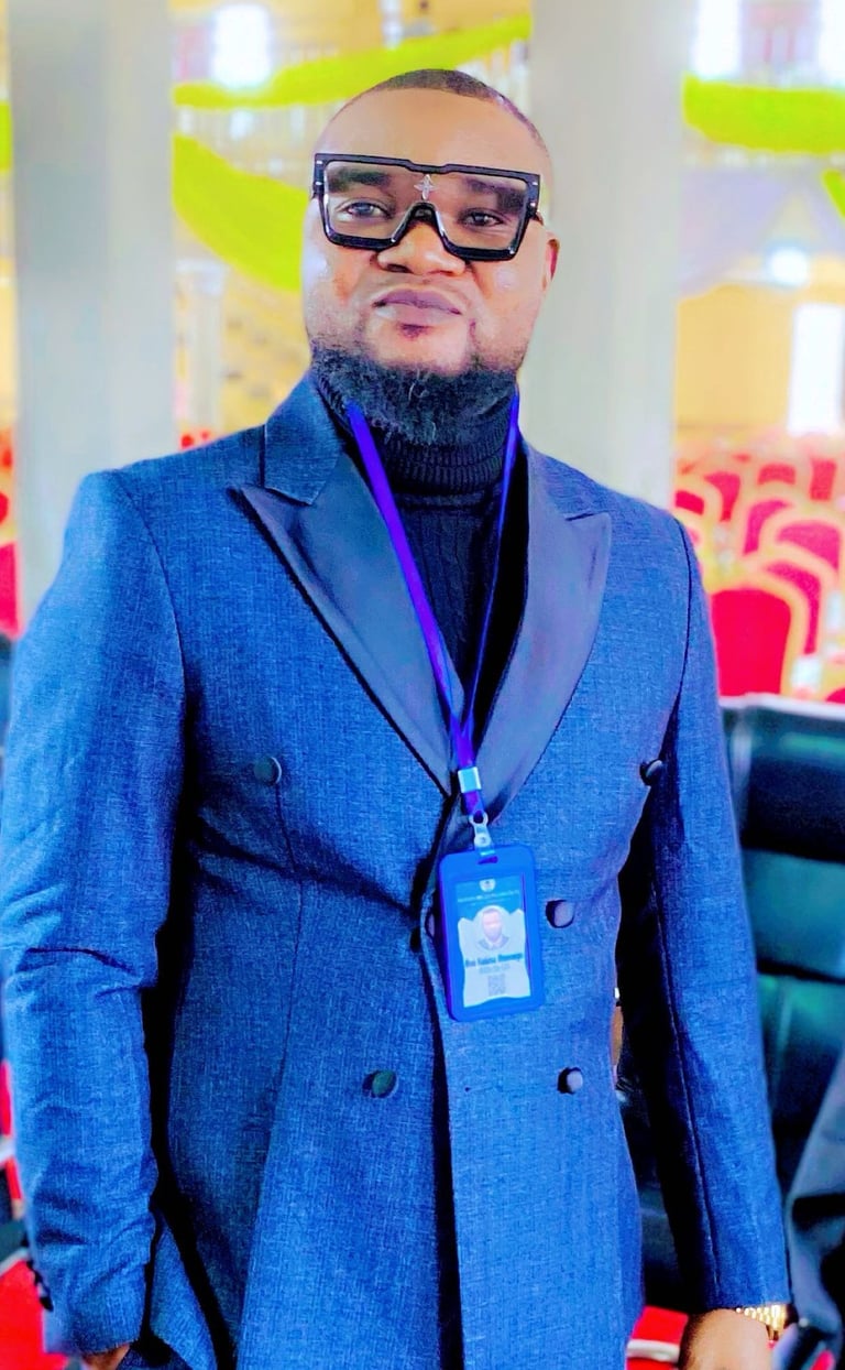A man wearing a blue double-breasted suit and stylish black glasses at a formal event.
