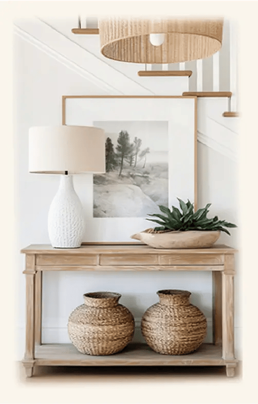 entrée intemporelle, console bois clair, pot en rotin dessous, plante verte, lampe blanche et tableau  dessus, suspension en 