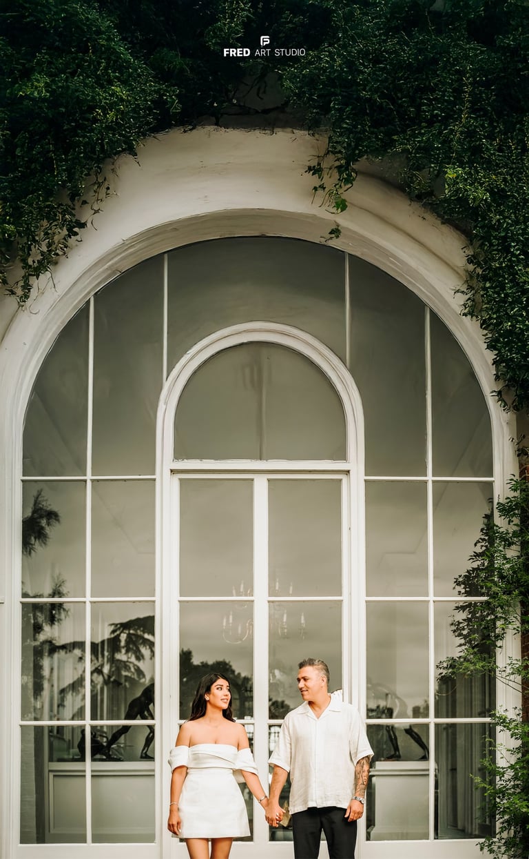Couple holding hands in front of large white window – engagement photography by Fred Art Studio