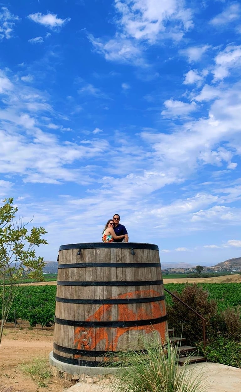 a couple sitting on a barrel of wine enjoying the view of the vineyards of Valle de Guadalupe