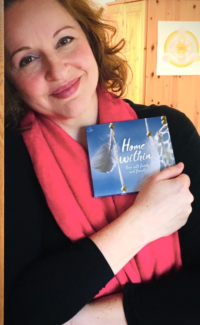 eine Frau lehnt am Türrahmen und hält eine CD im Arm, die den Titel "Home Within" trägt.