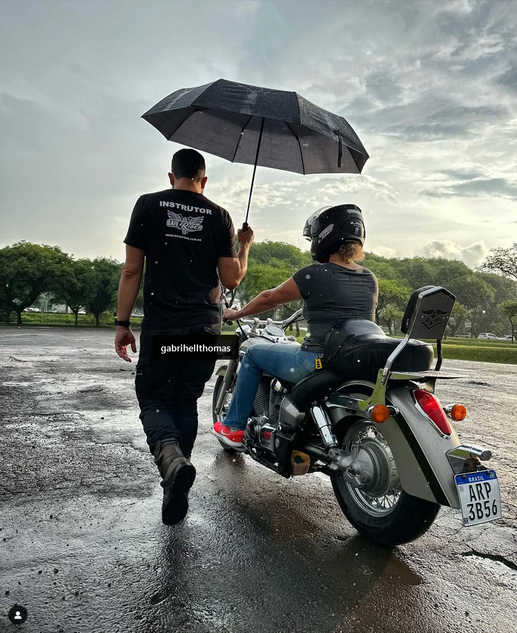 Instrutor segurando guarda chuva para pilota em moto