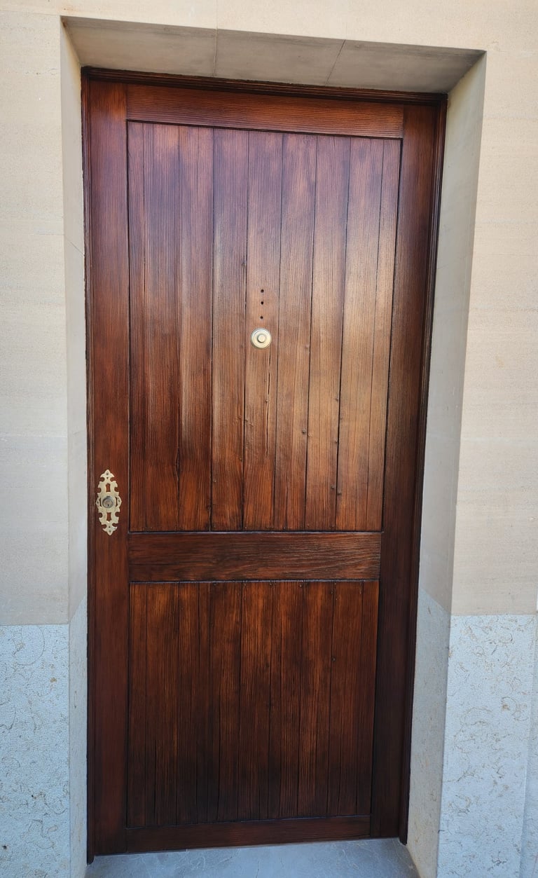 Rustic dark wood front door with vertical panels and brass hardware set in a stone archway.