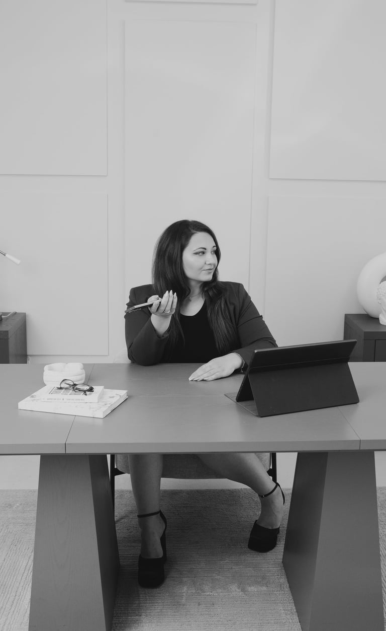 Adriana sitting at a desk with a tablet and phone in a modern office.