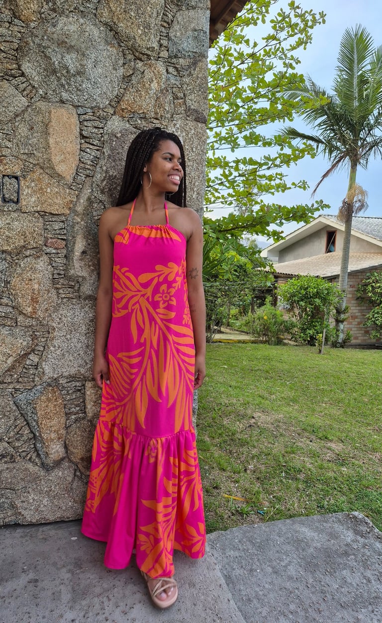 Mulher em pé usando um vestido com babado franzido, estampado nas cores rosa e laranja