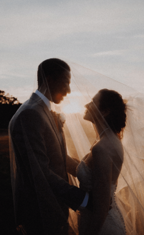 a bride and groom standing in front of a sunset