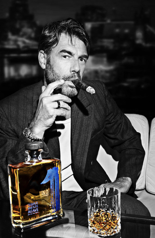 a man smoking a cigar with a bottle of uno tequila añejo