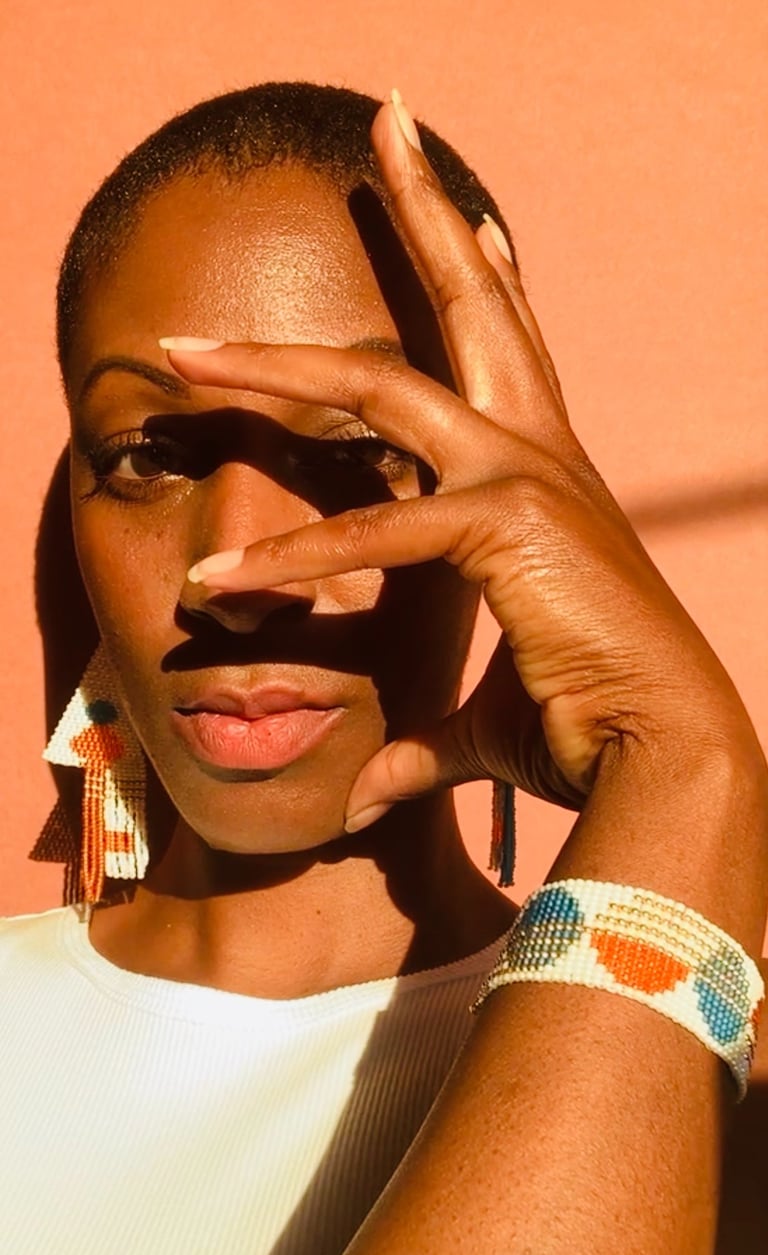 A black woman wearing a pair of matching beaded earrings and beaded bracelets