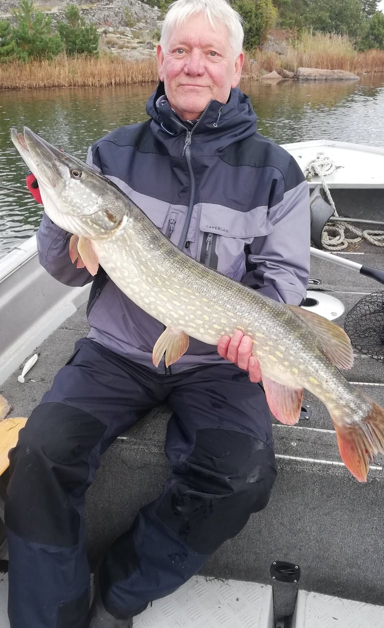 a man is sitting in a fishing boat in sweden, he caught a pike in sweden.