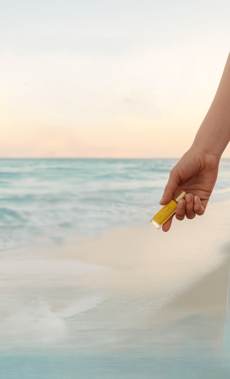 image of hand holding an essential oil bottle beachside
