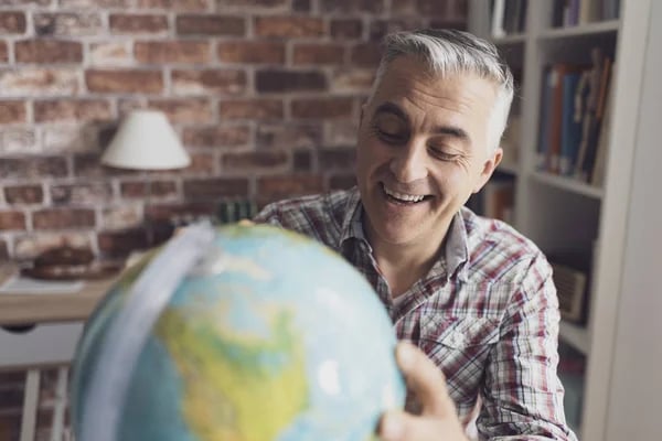 Homem sorridente segurando globo terrestre, representando expatriados e mobilidade global.