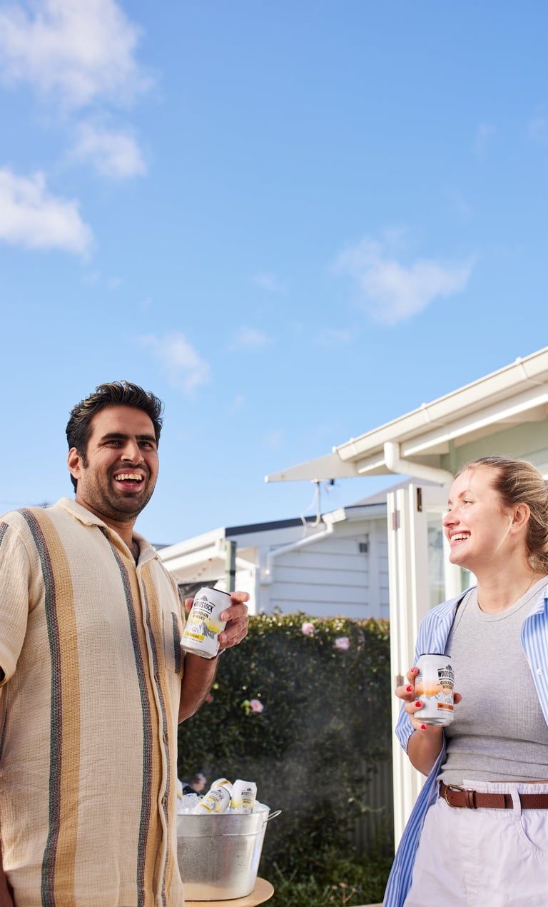 Product campaign photography - a man and woman standing outside of a house holding woodstock cans