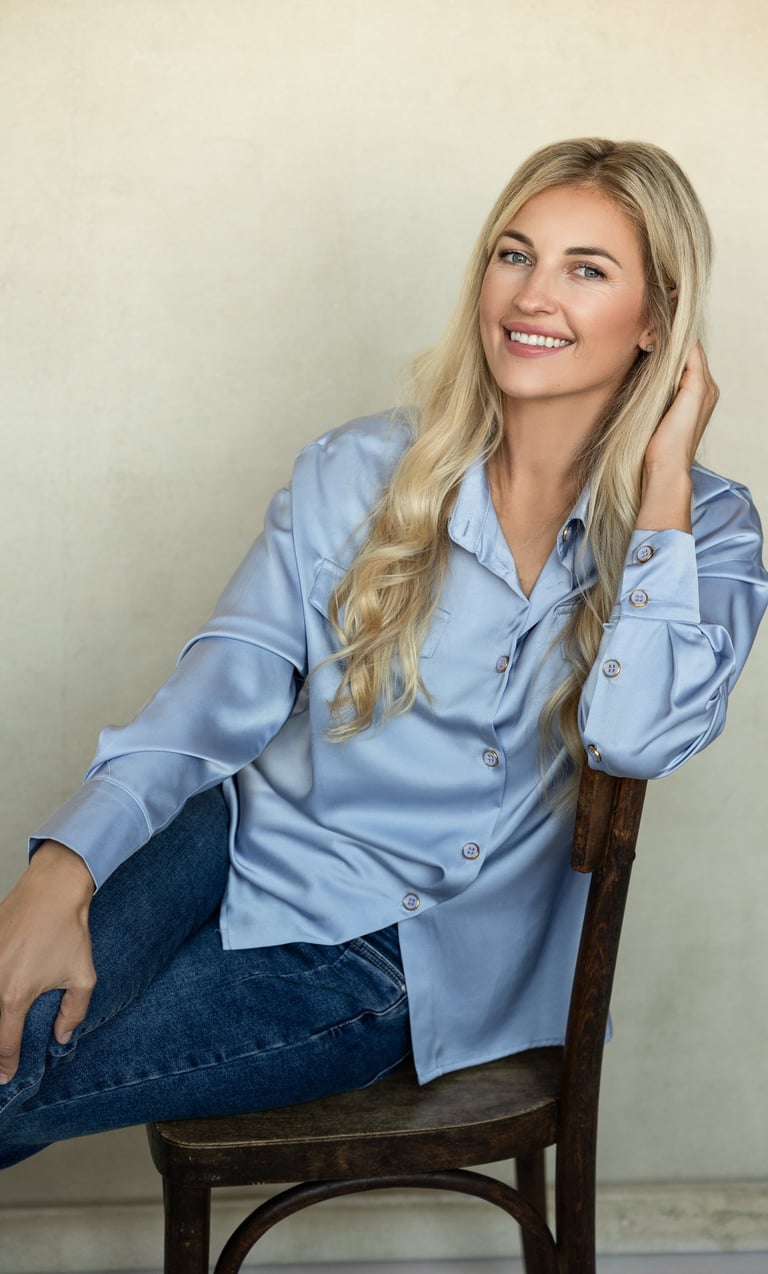 moteris human design koučerė sėdi ir šypsosi, apsirengusi žydros spalvos marškiniais