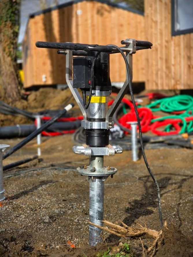 Portable hydraulic ground screw driver installing a steel pile foundation at a construction site.