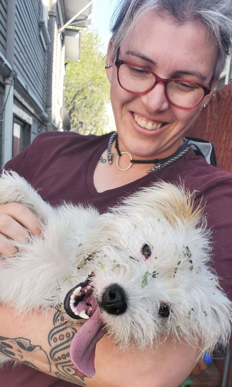 A tired, happy, messy puppy is lounging in a smiling persons arms, looking at the camera