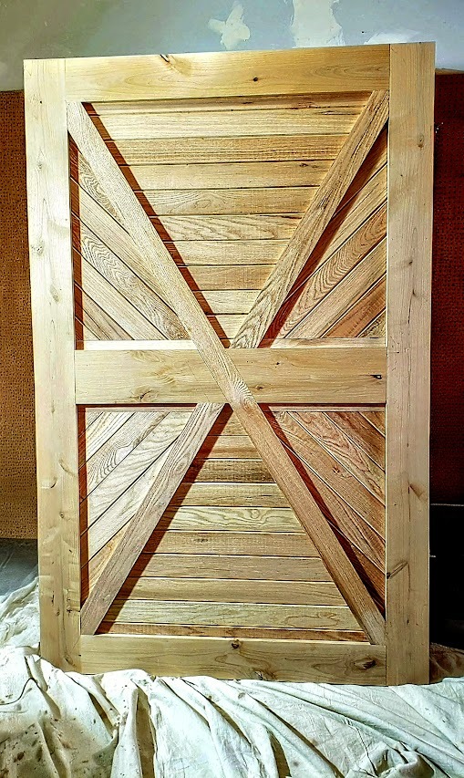 Handcrafted rustic sliding barn door made of light natural wood with a double X-brace design.