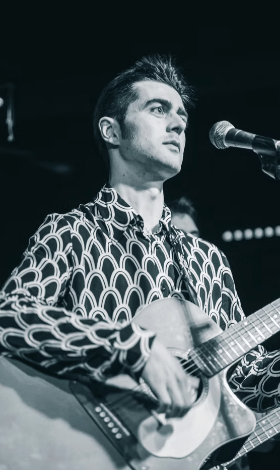 Rock and roll singer Olly Williams in Brighton, captured in black and white while performing with acoustic guitar.