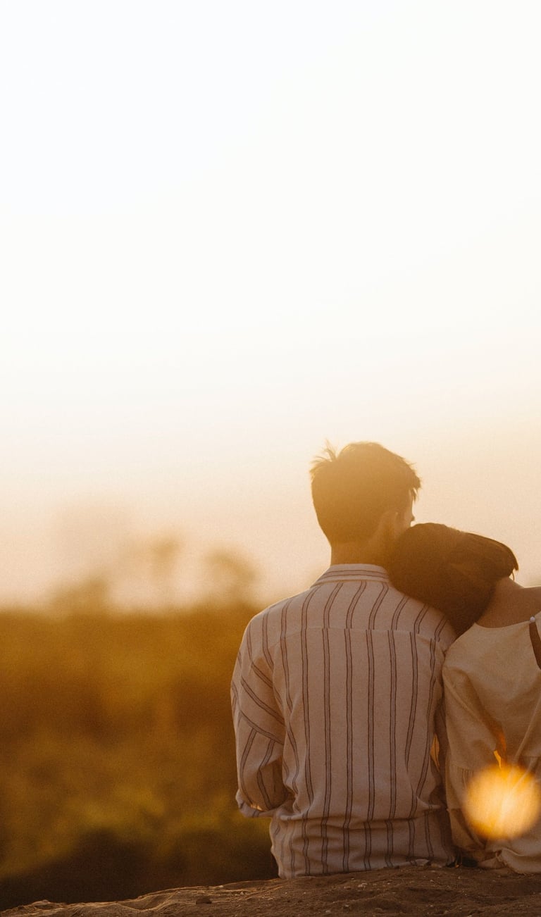 Couple de dos assis face à un paysage de soleil couchant.