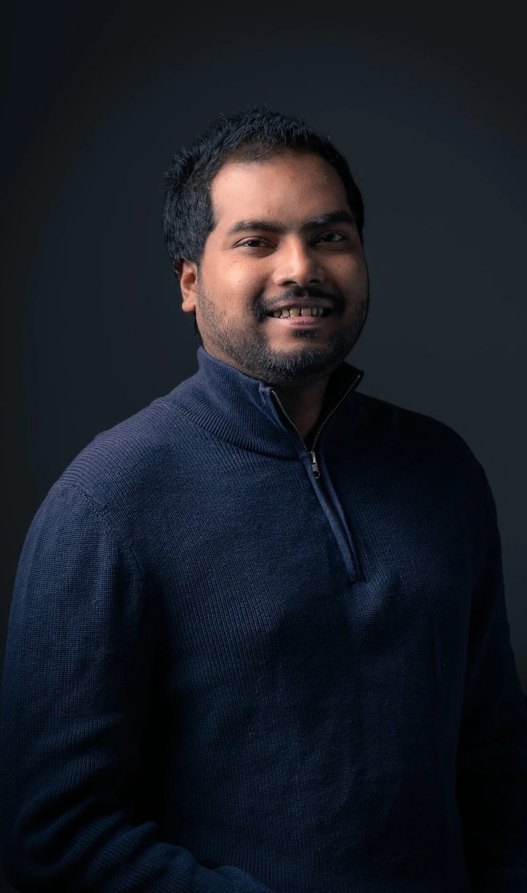 Professional headshot of Tharinda H.A smiling in a navy sweater against a dark gray background.