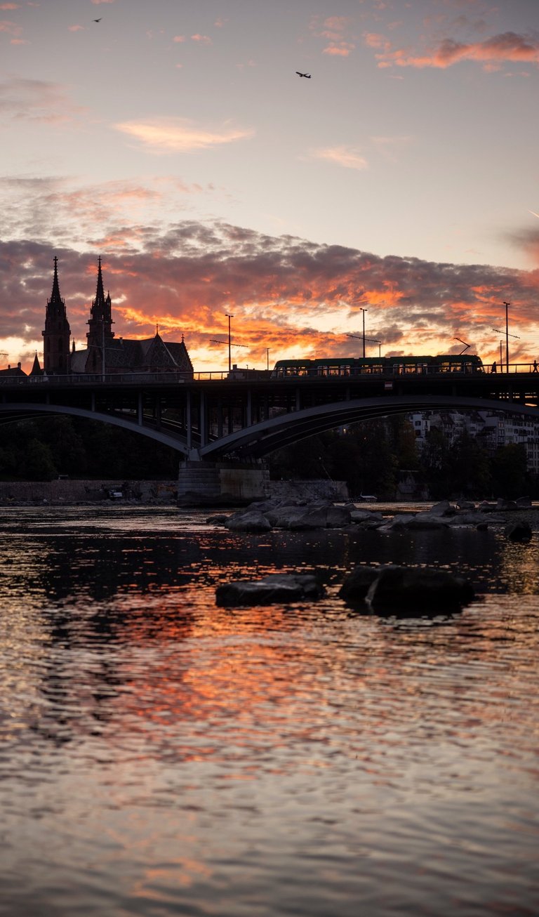 Sunset over Basel city skyline with a tram crossing the bridge near Basel Minster cathedral.