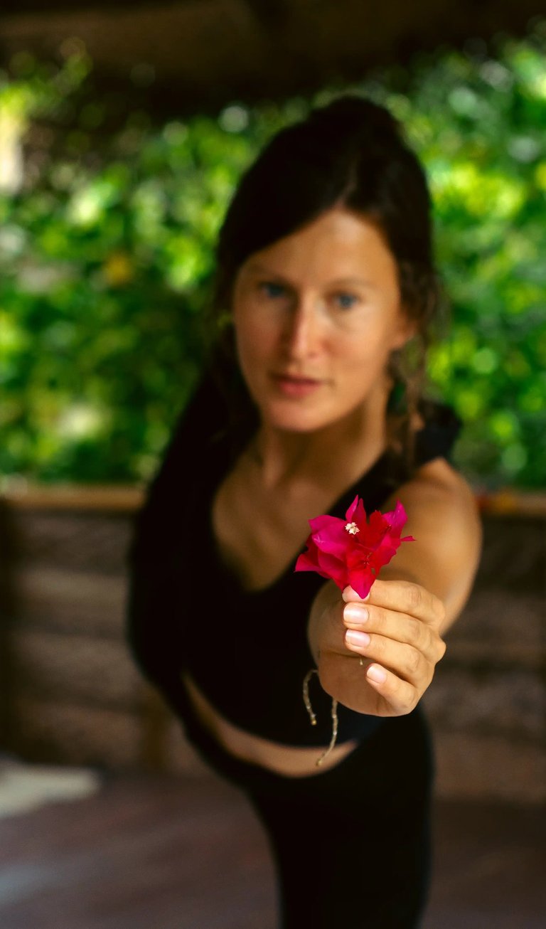 Yoga teacher in dancer pose holding flower with focus on blossom, mindful essentials