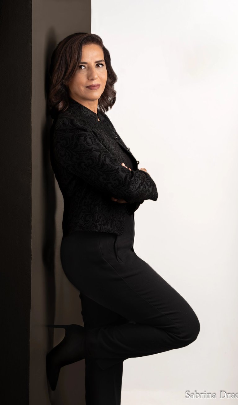 a woman leaning against a wall in a black shirt and black pants with high heels