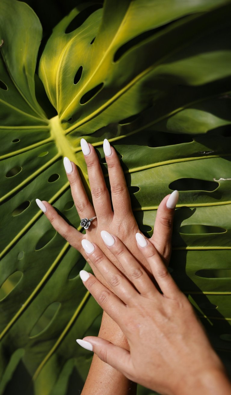 Manucure élégante en forme d'amande blanche sur une main ornée d'une bague rose argentée sur fond de