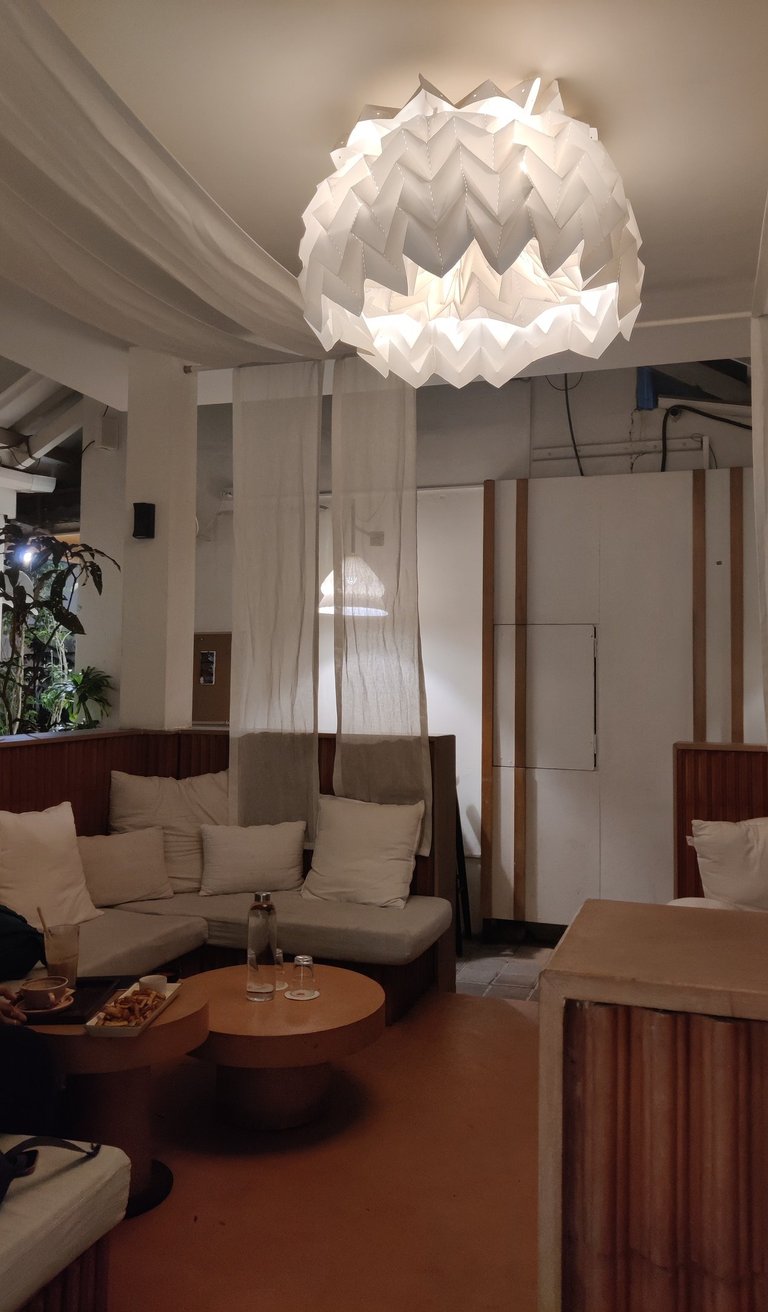 Cozy cafe interior featuring a geometric  light, white drapes, and comfortable lounge seating with pillows.