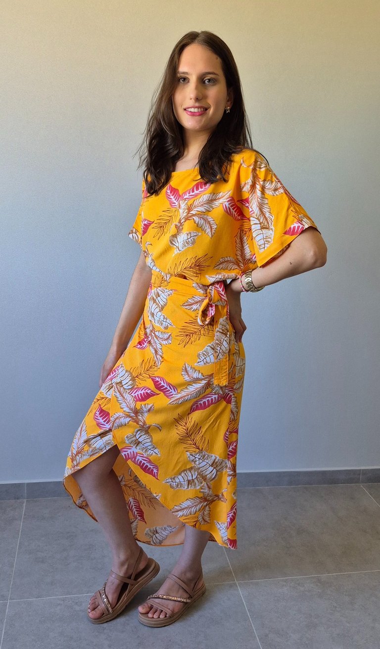 Mulher em pé usando uma saia envelope amarela, com estampa de folhas.