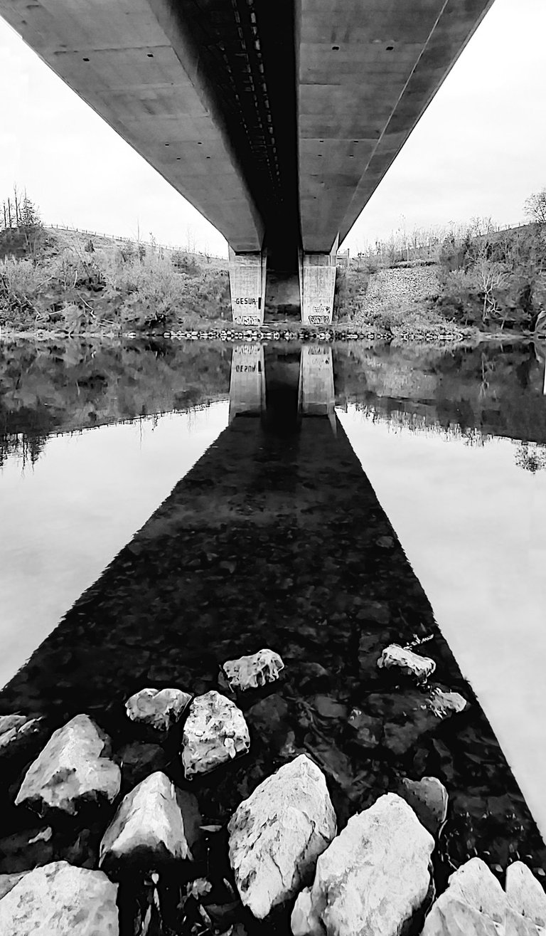 a bridge spanning a river with rocks and water and reflections