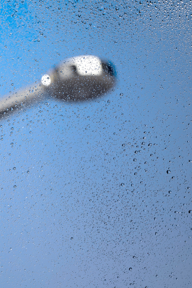 Water droplets on a shower glass panel with a blurred showerhead in an Auckland bathroom repaired by