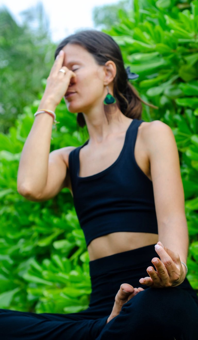 Woman practicing Nadi Shodhana pranayama seated before lush green, breathwork and pranayama