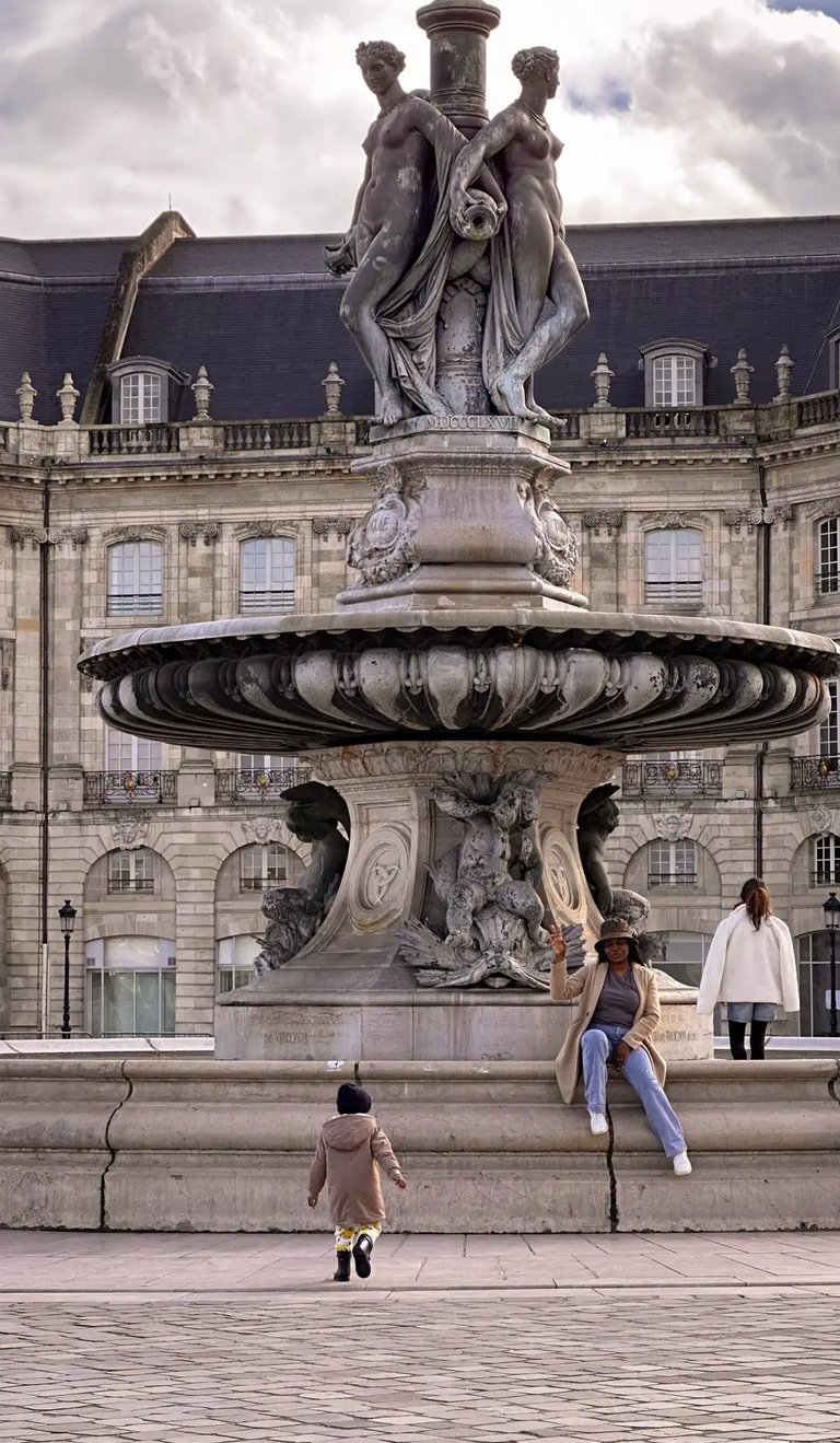 A woman sits on the Fountain of the Three Graces in Place de la Bourse, Bordeaux, France.