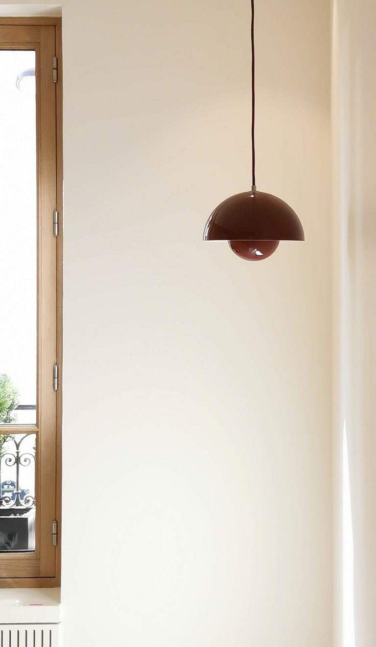 Dark brown dome-shaped pendant lamp hanging in a minimalist white room near a wooden window.