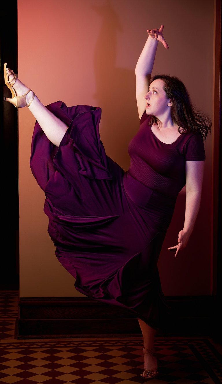 a woman in a purple dress with one leg up dancing in a latin dance style