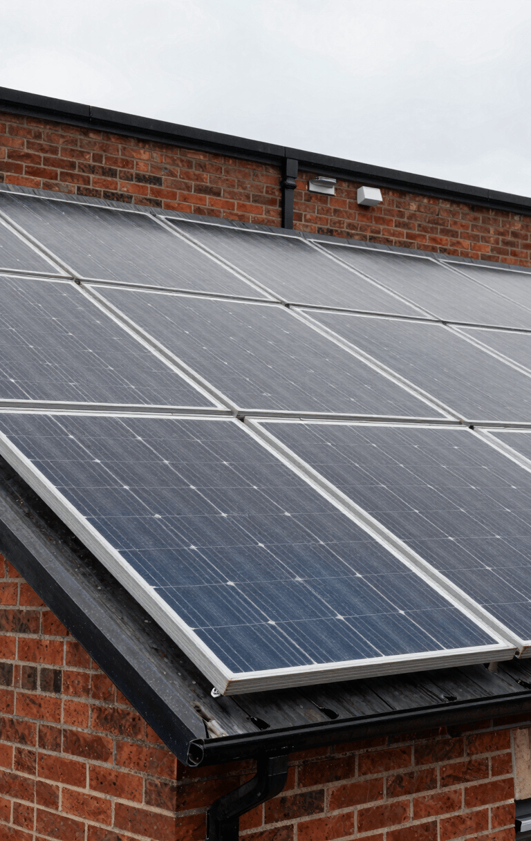 Close-up environmental shot of solar panels installed on a brick-faced UK commercial building, overcast sky above, guttering and flat roof edge visible, natural daylight, no people