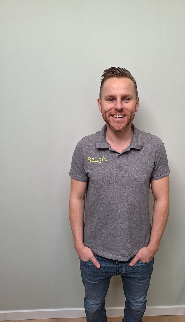 een man in een grijs shirt en broek die voor een muur staat