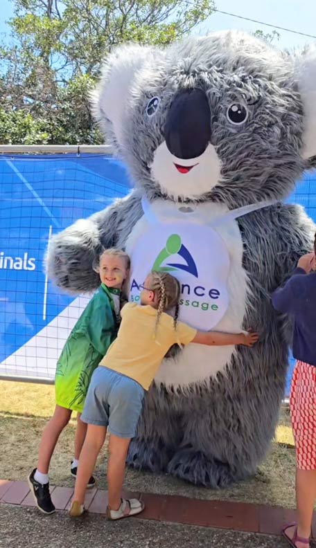 two children hugging a huge Advance Body Massage Koala Mascot
