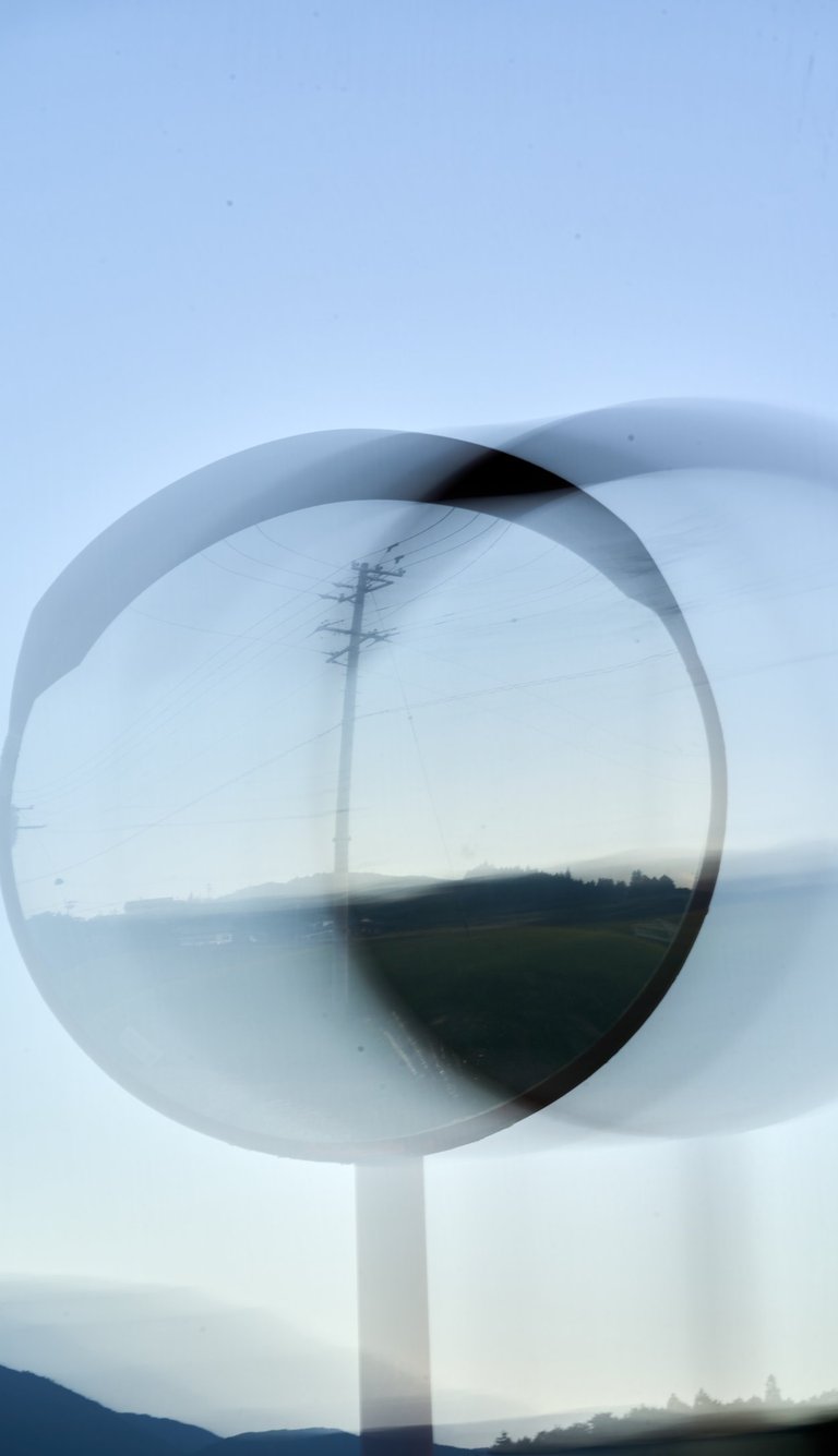 Double exposure artistic view of a convex traffic mirror reflecting an utility pole and rural landscape.