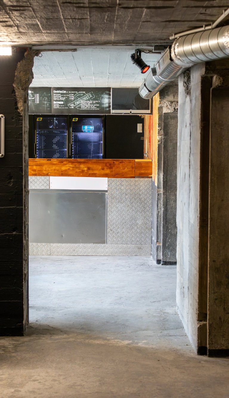 Industrial underground bar with concrete walls, metal counters, and a chalkboard drink menu.