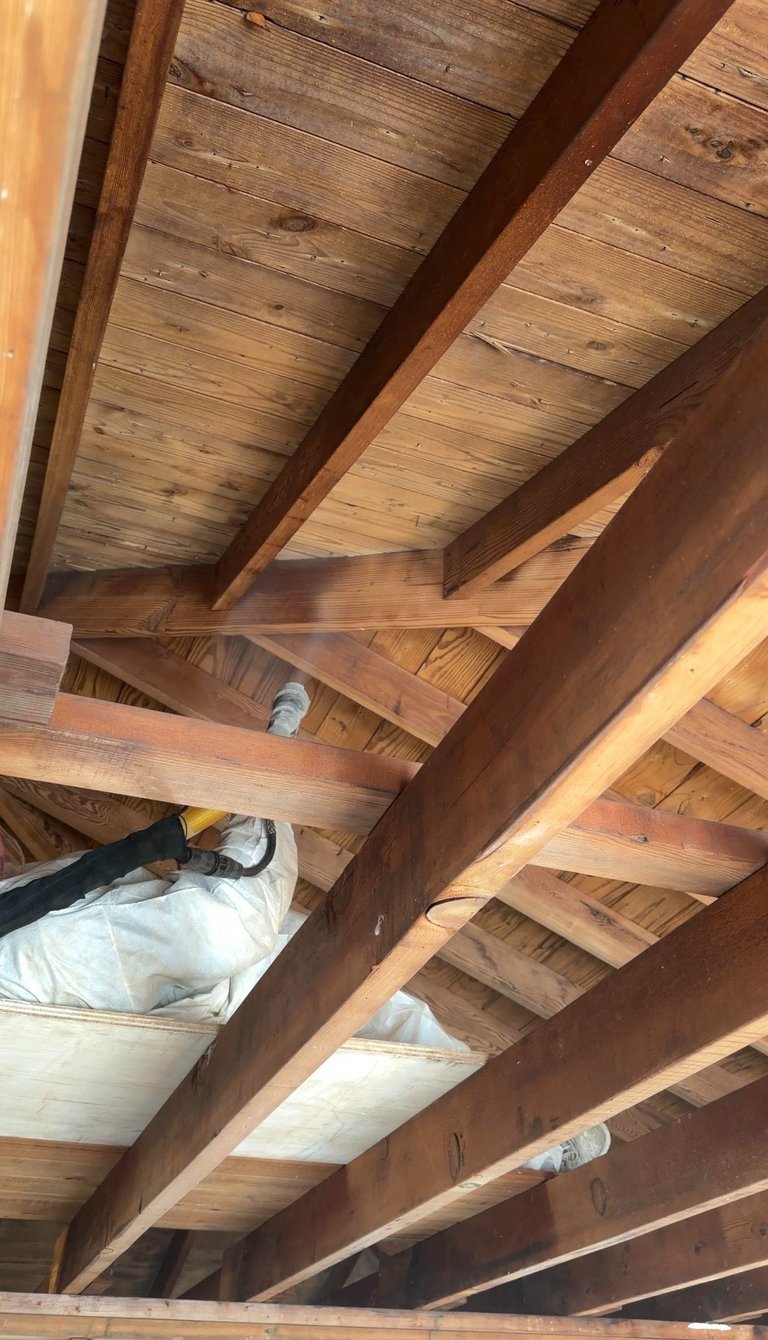 A worker in a white suit using a dry ice blaster to restore wood ceiling beams in an attic.