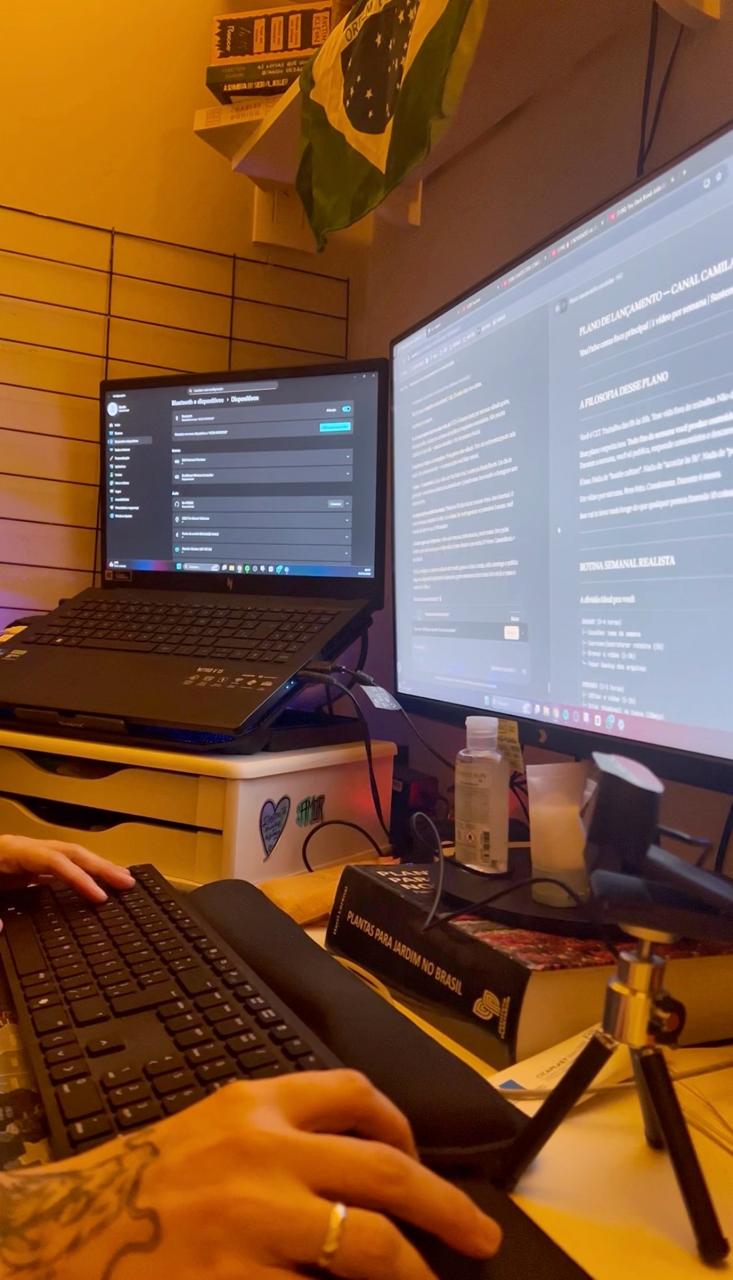 Dual monitor home office setup with a laptop, keyboard, and Brazilian flag on the wall.