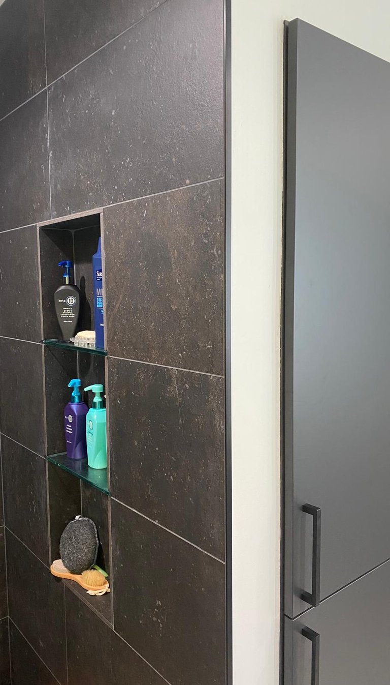 Modern bathroom shower with dark large-format tiles and a recessed wall niche with glass shelves for toiletries.