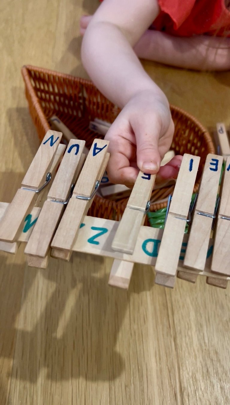 A child practices fine motor skills using wooden clothespins with letters for a DIY alphabet matching activity.