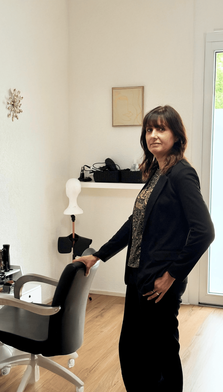 Femme debout à côté d’un fauteuil dans une pièce lumineuse, décorée de façon simple et élégante.