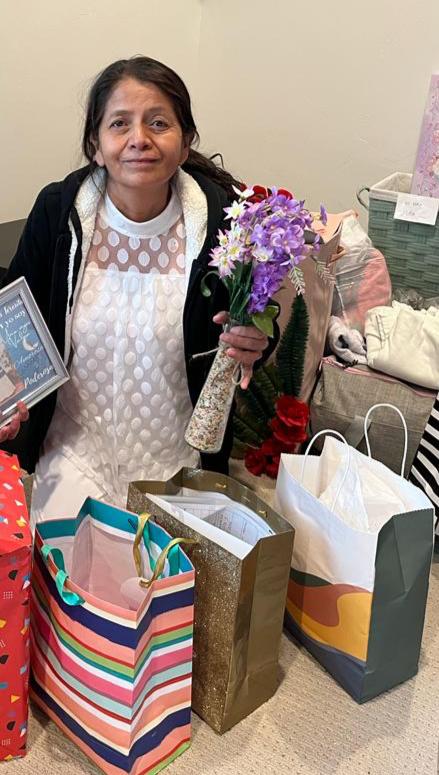 Smiling woman holding purple artificial flowers and gifts for a special celebration.