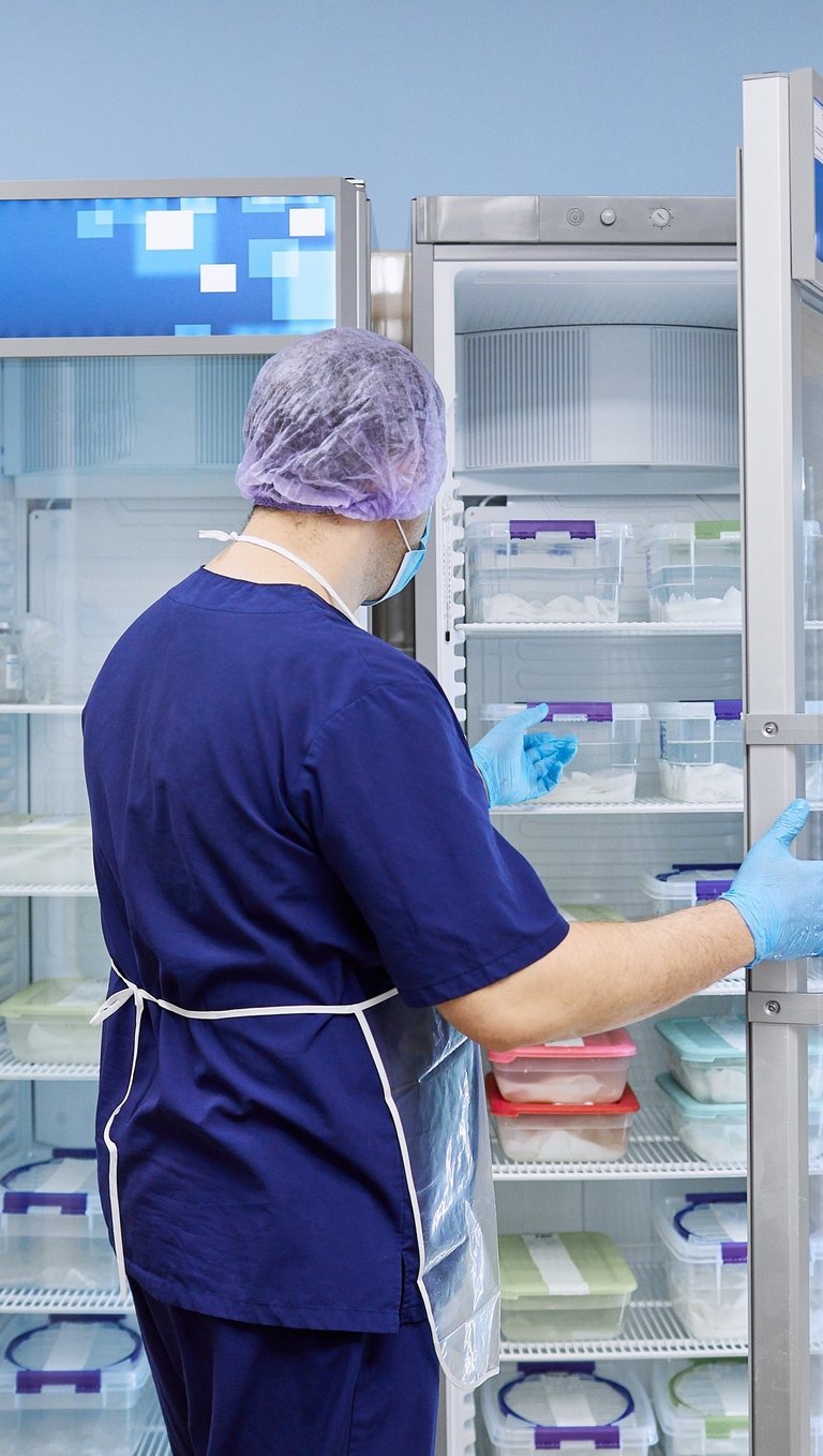 Laboratory technician in blue scrubs organizing samples in a medical laboratory refrigerator.